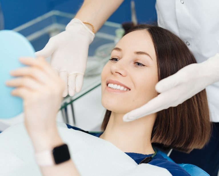 Perfect smile, woman looking in the mirror. Visit at the dentist